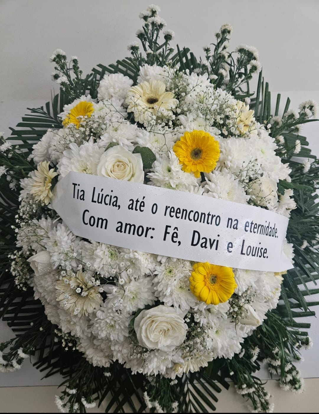 Coroa de flores brancas e amarelas com faixa personalizada